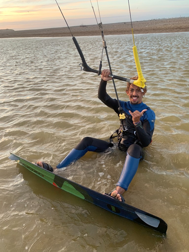 Kitesurfer in shallow water at Essaouira beach at sunset, holding kite bar and shaka sign