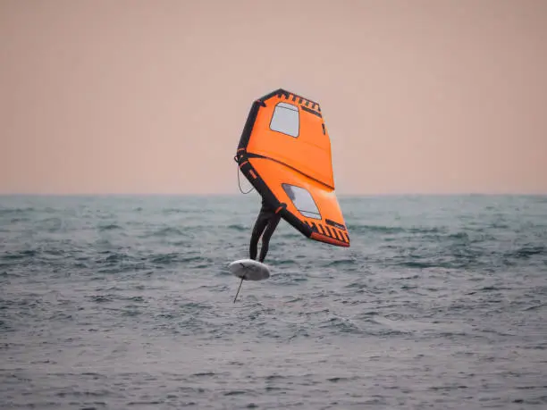 Wing foiler jumping above the Atlantic at Essaouira with orange wing against golden sky