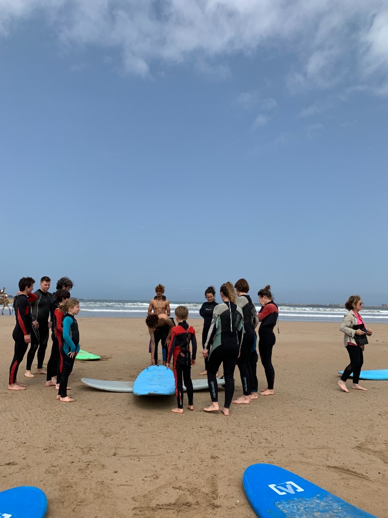 Kids surf lessons Essaouira — instructor teaching children on foam boards on the beach with camels in the background