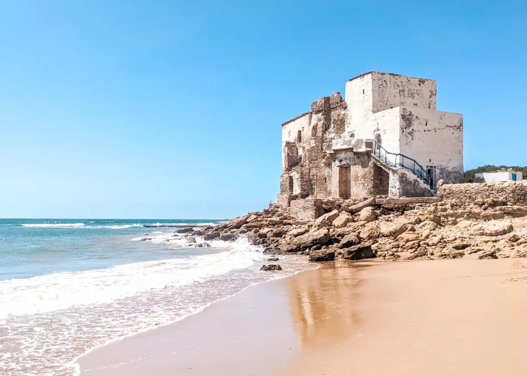 Historic white marabout building on the rocks at Sidi Kaouki beach with Atlantic waves
