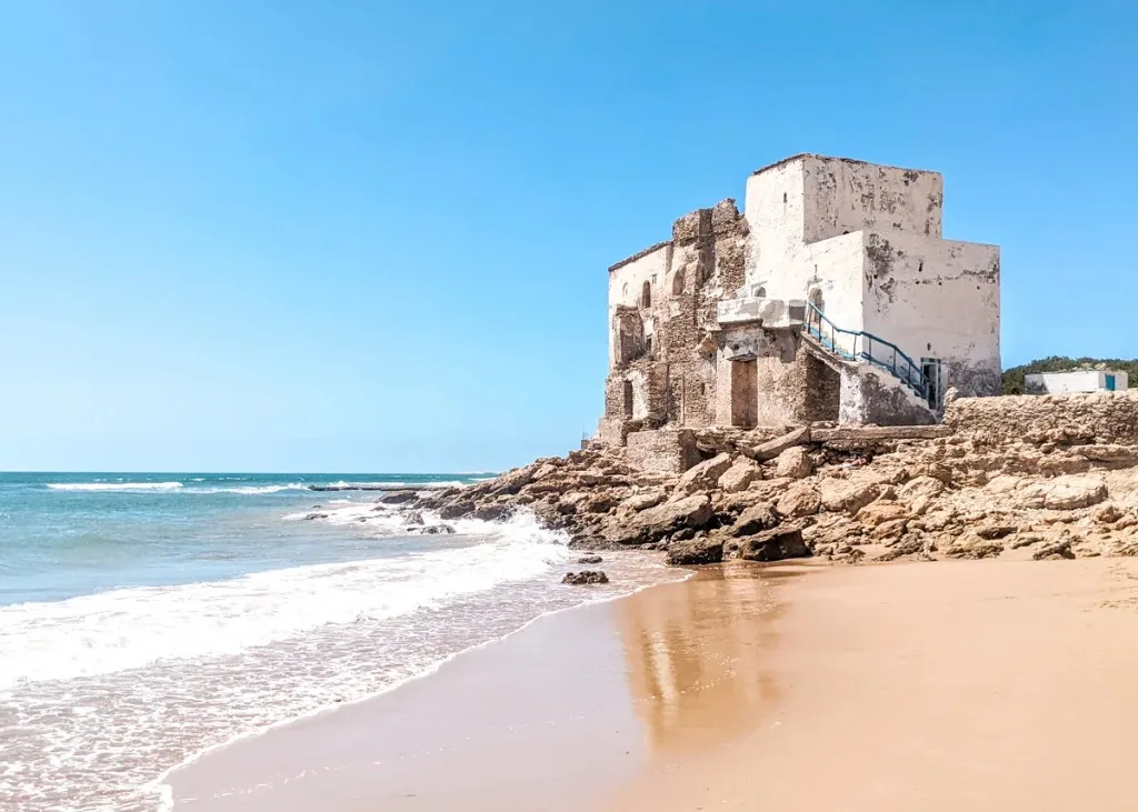 Historic white marabout building on the rocks at Sidi Kaouki beach with Atlantic waves