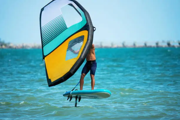Wing foiler foiling above turquoise Atlantic water at Essaouira with handheld wing