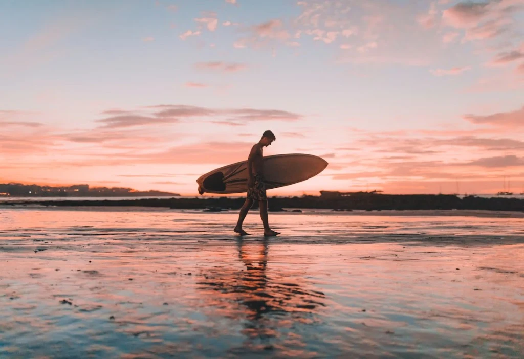 Surfer walking on Essaouira beach at sunset